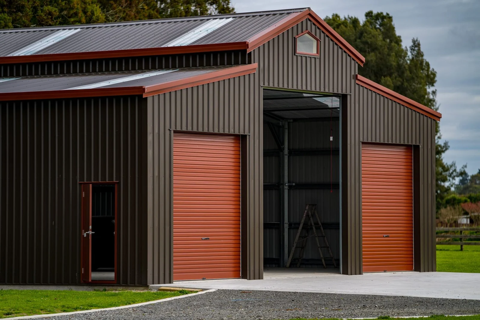 Dark steel-clad American barn with a raised centre roof, red trim, and tall roller-door bays